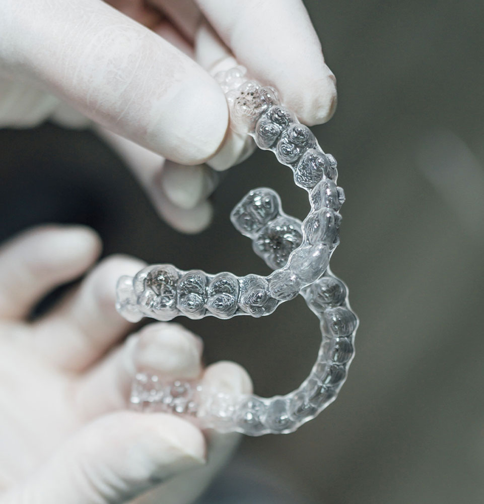 gloved hands holding clear aligners