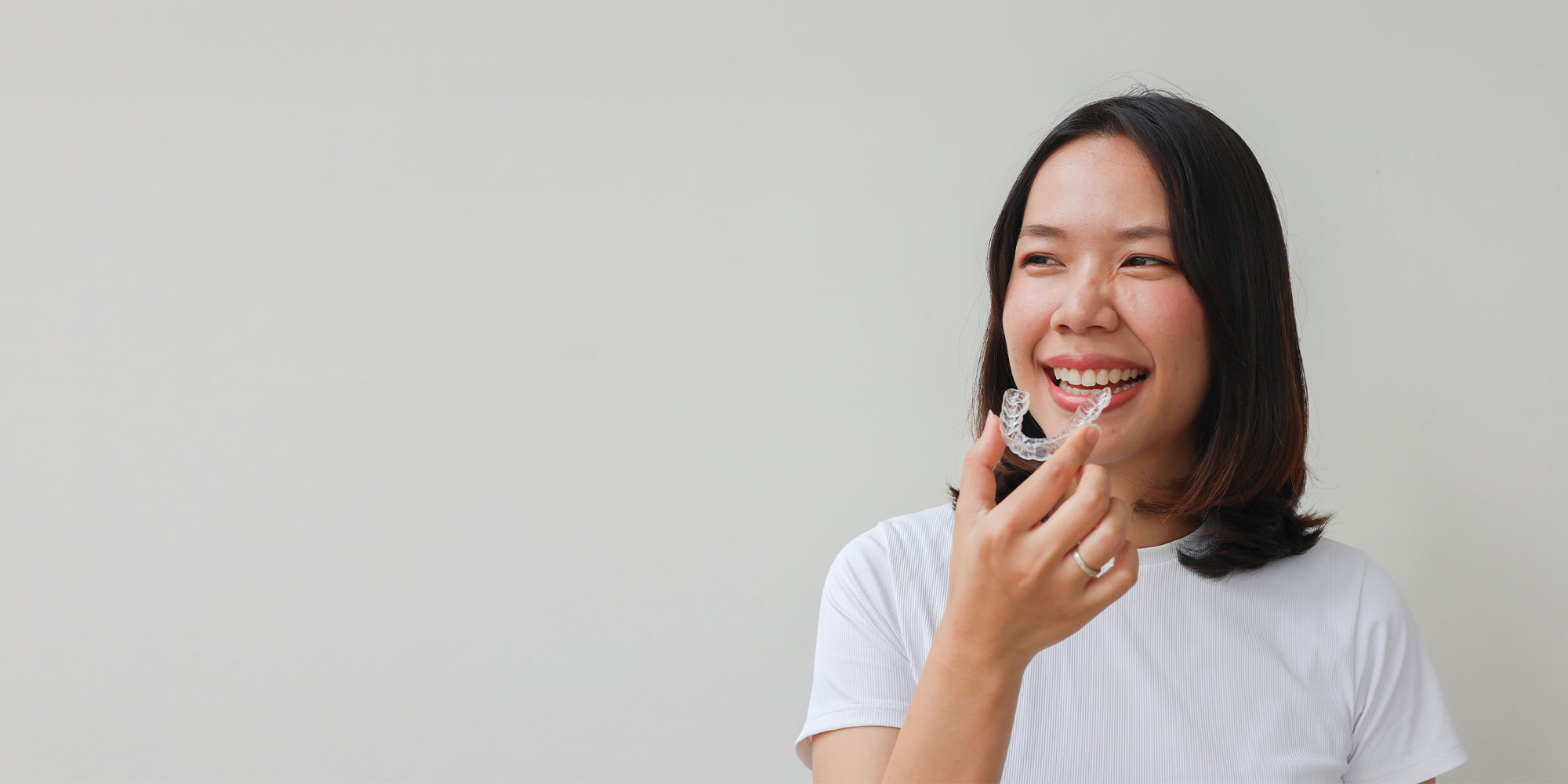dental patient smiling and holding clear aligners up to her mouth