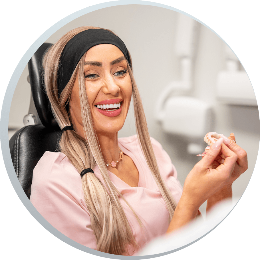 Lacie - dental implant patient smiling and holding full arch dental implant model